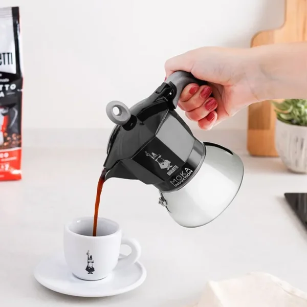 קפה חם נמזג ממקינטה ביאלטי מוקה אינדוקציה שחורה 4 כוסות לתוך ספל.