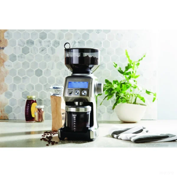 מטחנת קפה Sage Smart Grinder Pro SCG820 בנירוסטה מוברשת על שיש מטבח, טוחנת אל מיכל הקפה הטחון לצד שקית פולים