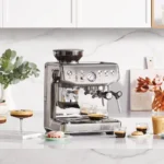 מכונת אספרסו Sage Barista Express Impress SES876 במטבח לבן, לצד מבחר משקאות קפה