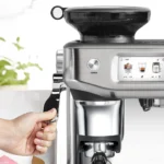 מסך המגע של מכונת Sage Barista Touch Impress SES882 מציג הכנת לאטה, לצד ידית החליטה מתחת ליציאת הטחינה