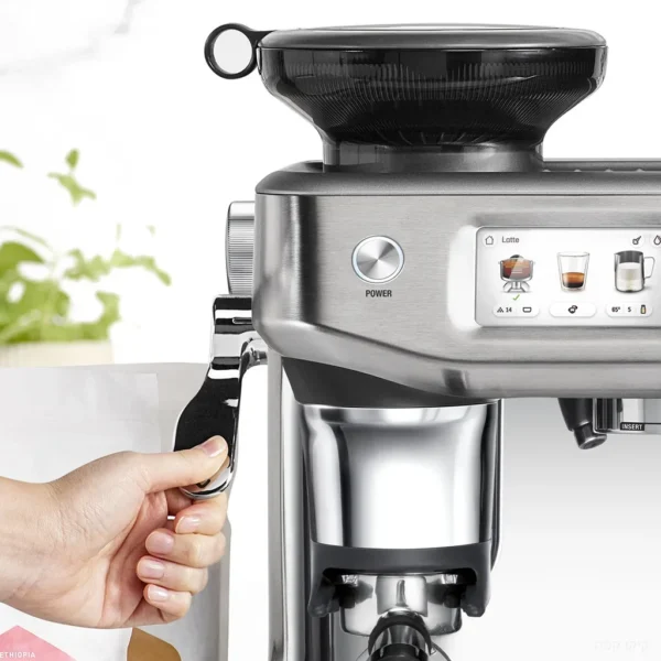 מסך המגע של מכונת Sage Barista Touch Impress SES882 מציג הכנת לאטה, לצד ידית החליטה מתחת ליציאת הטחינה
