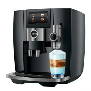 מכונת קפה אוטומטית Jura J10 Piano Black, מבט קדמי בזווית על רקע בהיר עם משקה חלב שכבתי בכוס זכוכית
