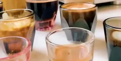 כמה משקאות קפה זה לצד זה בכוסות זכוכית שקופות, מכוס אספרסו קטנה ועד כוס גדולה עם חלב, על השיש ליד מכונת אספרסו
