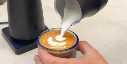 אמוץ סלע מוזג חלב מוקצף מכד FlowTip שחור לכוס אספרסו ויוצר לאטה ארט, לצד מקציף חלב חשמלי NanoFoamer PRO על הדלפק